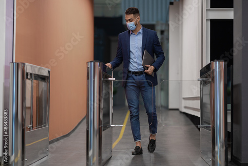 Man in face mask holding laptop, passing through entrance gate photo