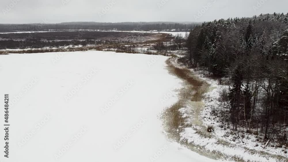 Aerial drone view of a frozen lake next to a forest in winter. Recorded in Tammeluha hiking trail in Estonia. Aerial drone view of a frozen lake next to a forest in winter. Recorded in Tammeluha hiking trail in Estonia.