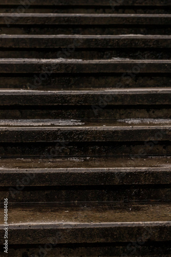 Vertical close-up photo of dark, wet, concrete set of steps at winter. Old weathered stone stairs texture for background. Pattern of vintage stairway. Urban lines in the city. 