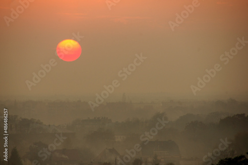 Zachód słońca nad spowitym w smogu miastem.