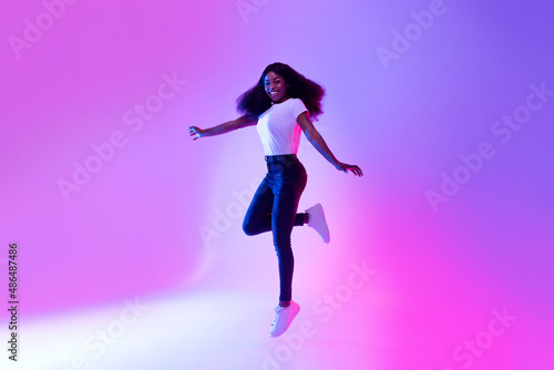 Full length portrait of active energetic millennial African American woman jumping in neon light, copy space