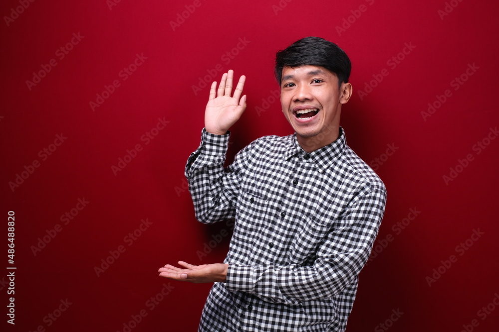 asian man wearing plaid shirt with happy expression showing empty space, on red background asian man wearing plaid shirt with happy expression showing empty space, on red background