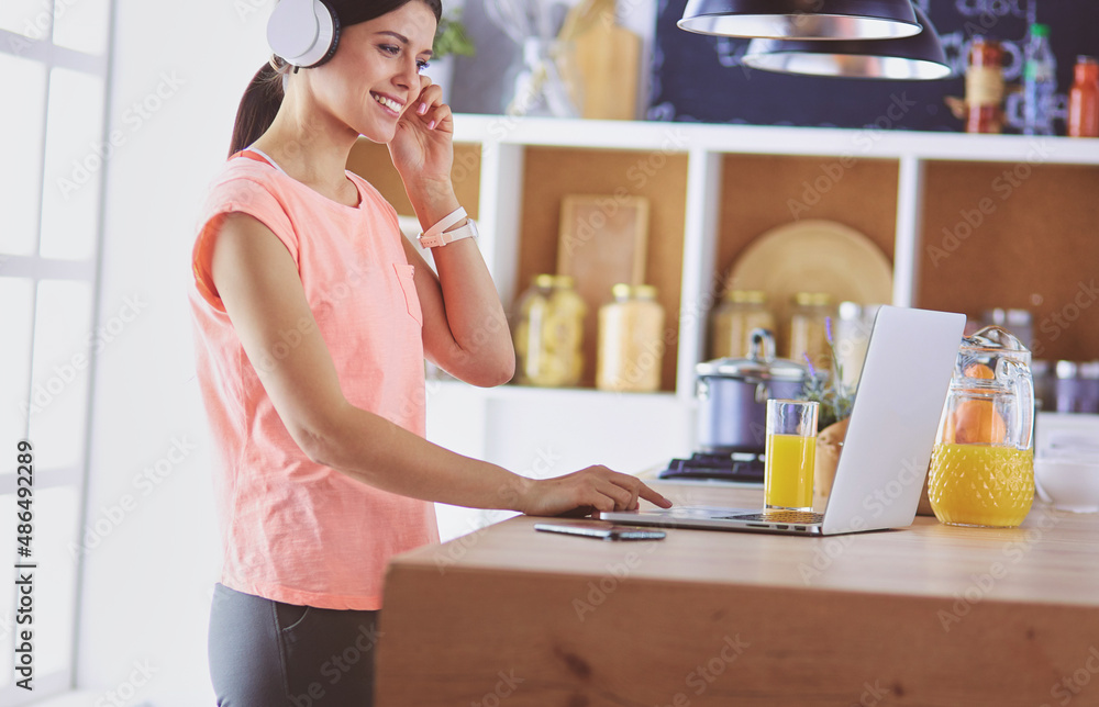 Young woman in kitchen with laptop computer looking recipes, smiling. Food blogger concept. Young woman in kitchen with laptop computer looking recipes, smiling. Food blogger concept.