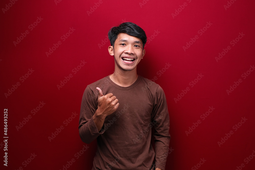asian man on red background wearing brown t-shirt pointing to empty space asian man on red background wearing brown t-shirt pointing to empty space