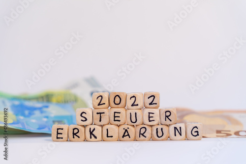 2022 German word for tax return, STEUERERKLÄRUNG, spelled with wooden letters wooden cube on a plain white background with banknotes, concept image  photo