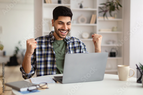 Arabic man using laptop celebrating success shaking fists screaming yes