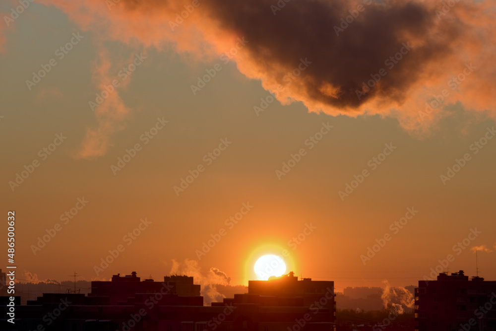 Naklejka premium Cityscape at sunset . The sun sets over the horizon over the rooftops. Photo of the city in the golden hour.