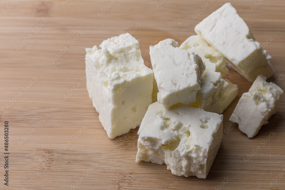Soft white cheese cubes on wooden board with copy space