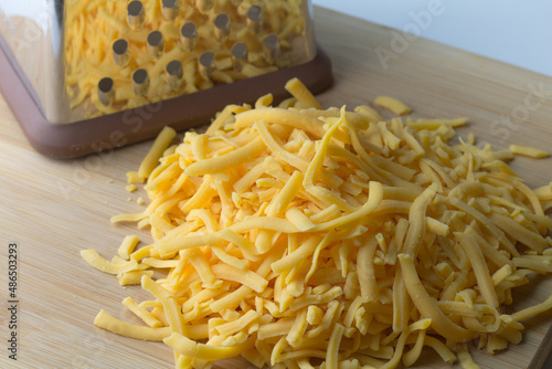 Grated cheddar cheese heap with cheese shredder in background
