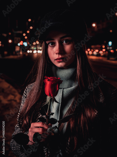 A woman smelling a rose against a night highway. Concept of love, dating and romantic dreams