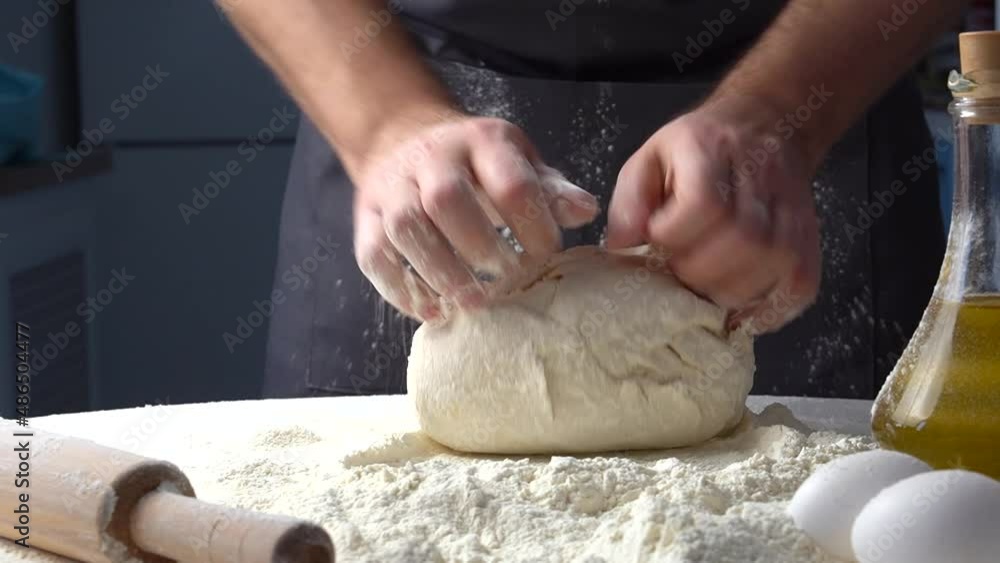 Male hands kneading dough with flour on kitchen table. Chef cooks dough in slow motion front view Male hands kneading dough with flour on kitchen table. Chef cooks dough in slow motion front view