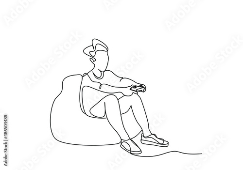 a young person sitting on a pear puff sofa plays with a console in his hand with his full body visibly