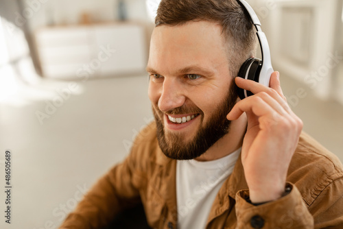Cheerful Guy Listening To Music Online Wearing Earphones At Home