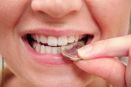 Zähne einer Frau beißen auf eine Euro-Münze photo