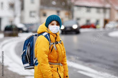 Little kid boy wearing medical mask on the way to school. Child backpack satchel. Schoolkid on cold autumn or winter day with warm clothes. Lockdown and quarantine time during corona pandemic disease