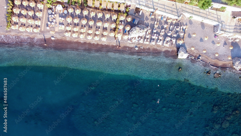 Aerial view of a empty beach at morning with straw umbrellas, people swimming in the sea. Drone view of a pebble beach. Transparent sea water with stones at the bottom.