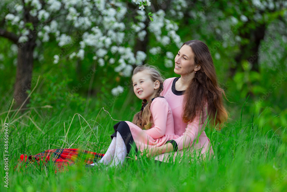 Fototapeta premium mother and daughter sit in the apple orchard in spring