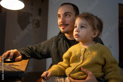 man working via laptop with his little toddler daughter on hands. Fatherhood, dad and daughter together