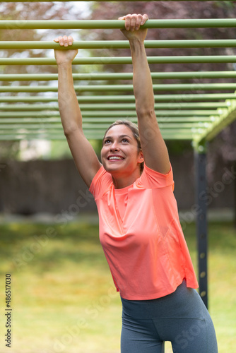 Strong blonde woman in an outdoor gym doing exercise in a structure cage
