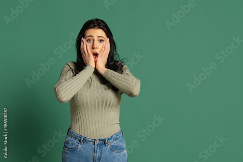 Surprised young beautiful girl wearing olive color sweatshirt isolated on green background. Concept of emotions, facial expression