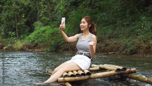 Young asian woman sitting on a bamboo raft making a video call , vlog using smartphone.