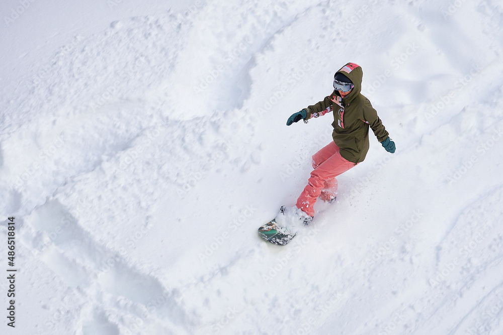 girl in helmet with glasses and tracksuit snowboarding down the mountain