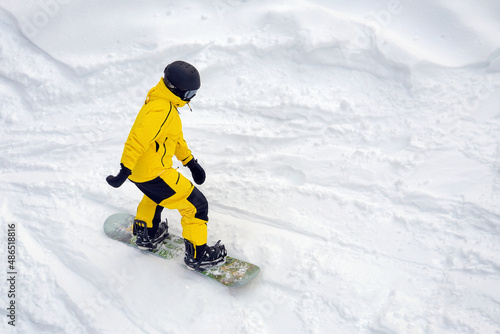 man in yellow tracksuit, helmet with glasses snowboarding downhill