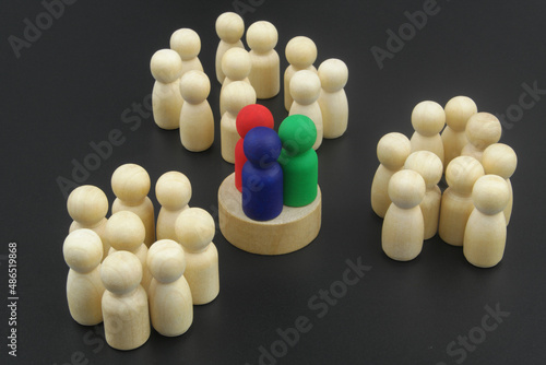 Three colored wooden figures as leaders standing near crowd of other figures. Concept of business leadership and elections.