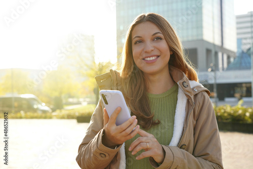 Smiling beautiful girl holding smartphone outside on sunset