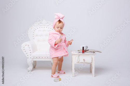 Fotografiet A cute little baby girl in a pink terry dressing gown with a chair and a mini dr