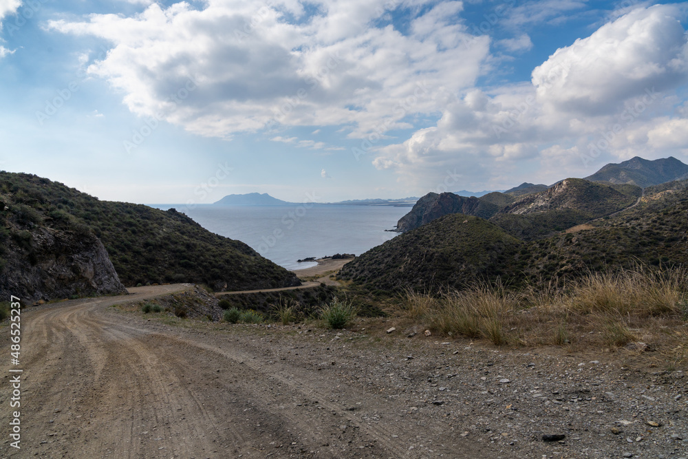 curvy dirt road leading down to a secluded beach on a wild and mountainous coastline