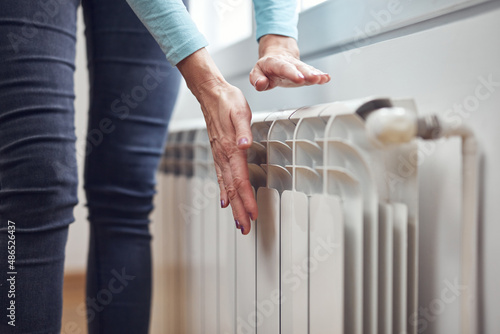 Woman heating her hands on the radiator during cold winter days.