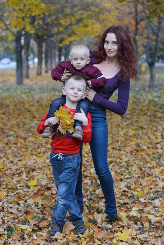 A young mother with her beloved sons in the park against the background of autumn foliage. Friendly family