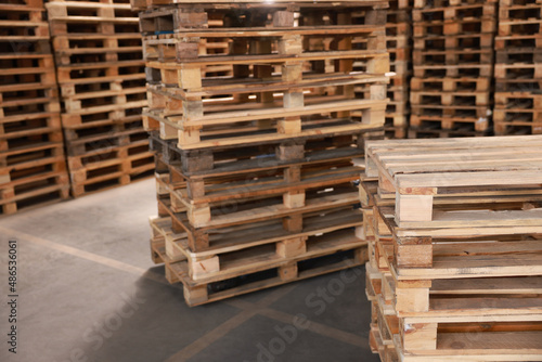 Many empty wooden pallets stacked in warehouse. Space for text