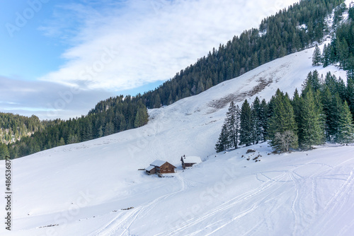 Isolated summer chalet and farm stables high up on the Swiss Alps covered in fresh powder snow near Bruelisau in Appenzell and skiers in the distance