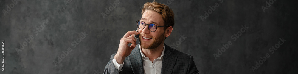 The smiling man talking on the phone while sitting in front of a laptop at a table in the studio The smiling man talking on the phone while sitting in front of a laptop at a table in the studio