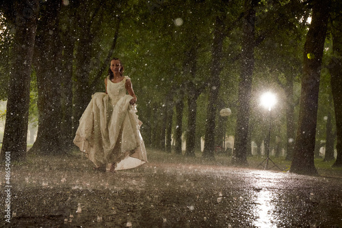 happy bride in a white wedding dress in the rain on an alley under big green trees walking peaying sitting and laughing photo