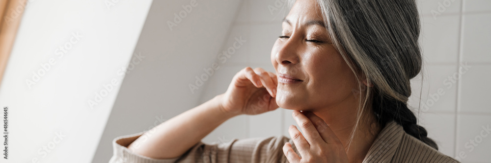 Mature grey woman smiling while getting facial massage in bathroom Mature grey woman smiling while getting facial massage in bathroom