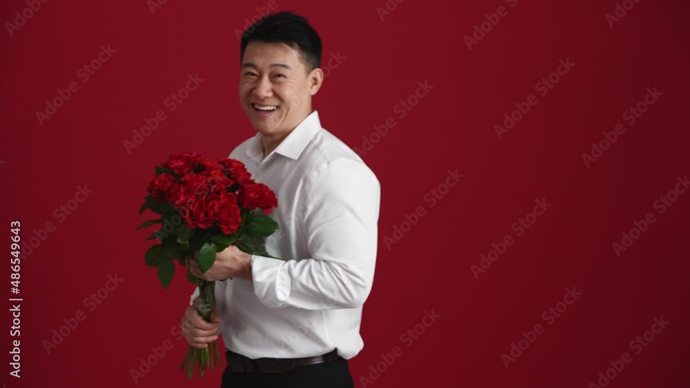 Smiling Asian man holding a bouquet of red roses and walking in the red studio Smiling Asian man holding a bouquet of red roses and walking in the red studio