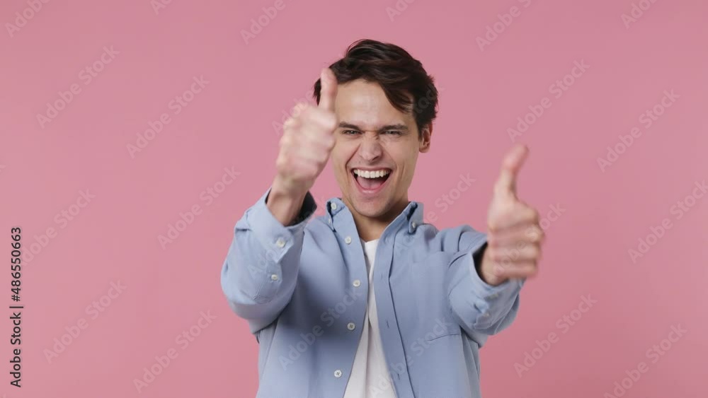 Excited cheerful vivid young brunet man 20s years old wears blue shirt looking camera showing thumb up like gesture isolated on plain pink background studio portrait. People emotions lifestyle concept Excited cheerful vivid young brunet man 20s years old wears blue shirt looking camera showing thumb up like gesture isolated on plain pink background studio portrait. People emotions lifestyle concept