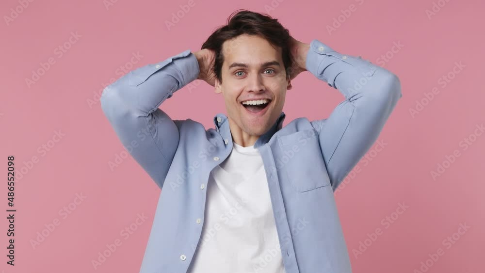 Excited young brunet man 20s wears blue shirt look camera surprised ask what wow omg no way doing winner gesture say yes celebrating put hands on face isolated on plain pink background studio portrait Excited young brunet man 20s wears blue shirt look camera surprised ask what wow omg no way doing winner gesture say yes celebrating put hands on face isolated on plain pink background studio portrait