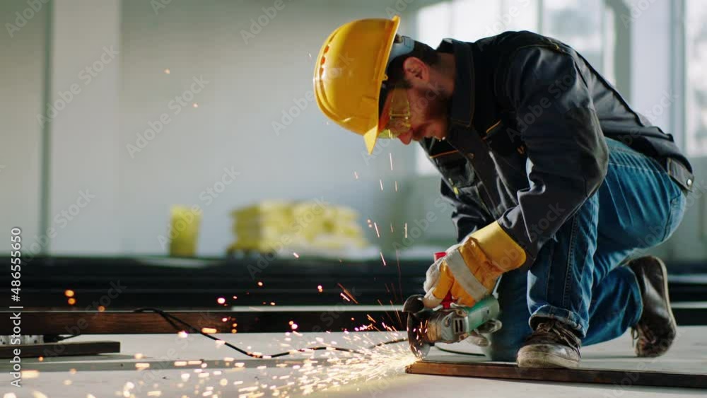 In the large building construction in front of the camera constructor worker using disc welding machine to cut some metals and creating the big sparks