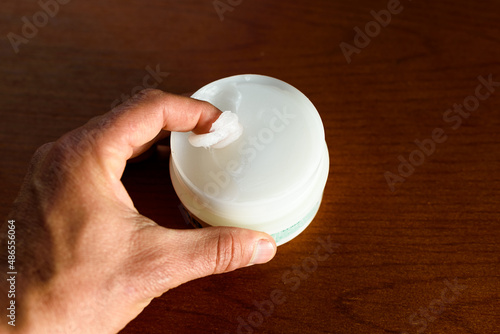 A man picks up white Vaseline to moisturize his skin, dark background.