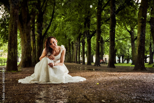 bride in white dress after rain completely wet on the ground on her knees between trees on a long path alley smiling praying shooting 