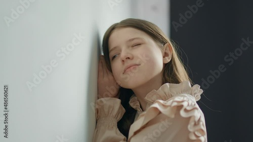 Blonde teen girl stands near a white wall and eavesdrops and smile photo