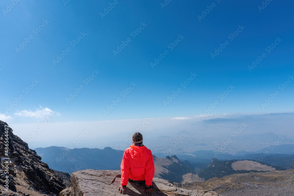 A young cheerful girl in a helmet, sits on the top of the mountain higher than clouds A young cheerful girl in a helmet, sits on the top of the mountain higher than clouds