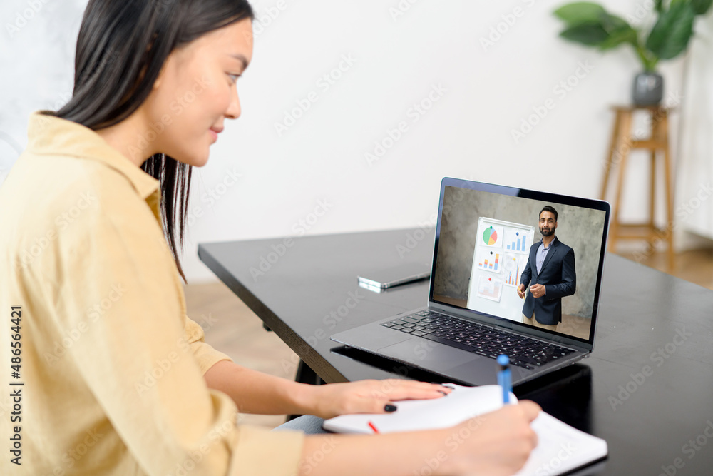 Female student studying online, takes notes, while male tutor, teacher talking on the laptop screen. Asian woman watching webinar, online training and writing with pen, e-study Female student studying online, takes notes, while male tutor, teacher talking on the laptop screen. Asian woman watching webinar, online training and writing with pen, e-study