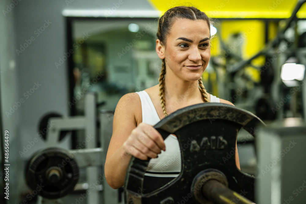 One adult caucasian woman female athlete putting weight plate on the barbel at gym during training bodybuilding and fitness weight lifting concept copy space waist up One adult caucasian woman female athlete putting weight plate on the barbel at gym during training bodybuilding and fitness weight lifting concept copy space waist up