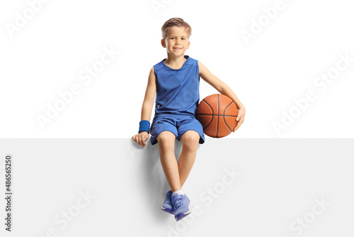 Smiling boy in a jersey holding a basketball and sitting on a blank panel