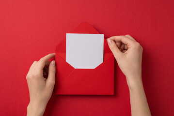 First person top view photo of valentine's day decorations female hands taking letter out of red envelope on isolated red background with blank space